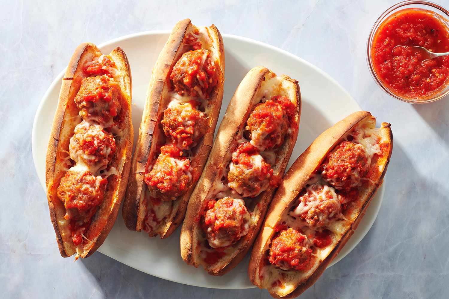 Meatball subs on a serving platter with extra tomato sauce