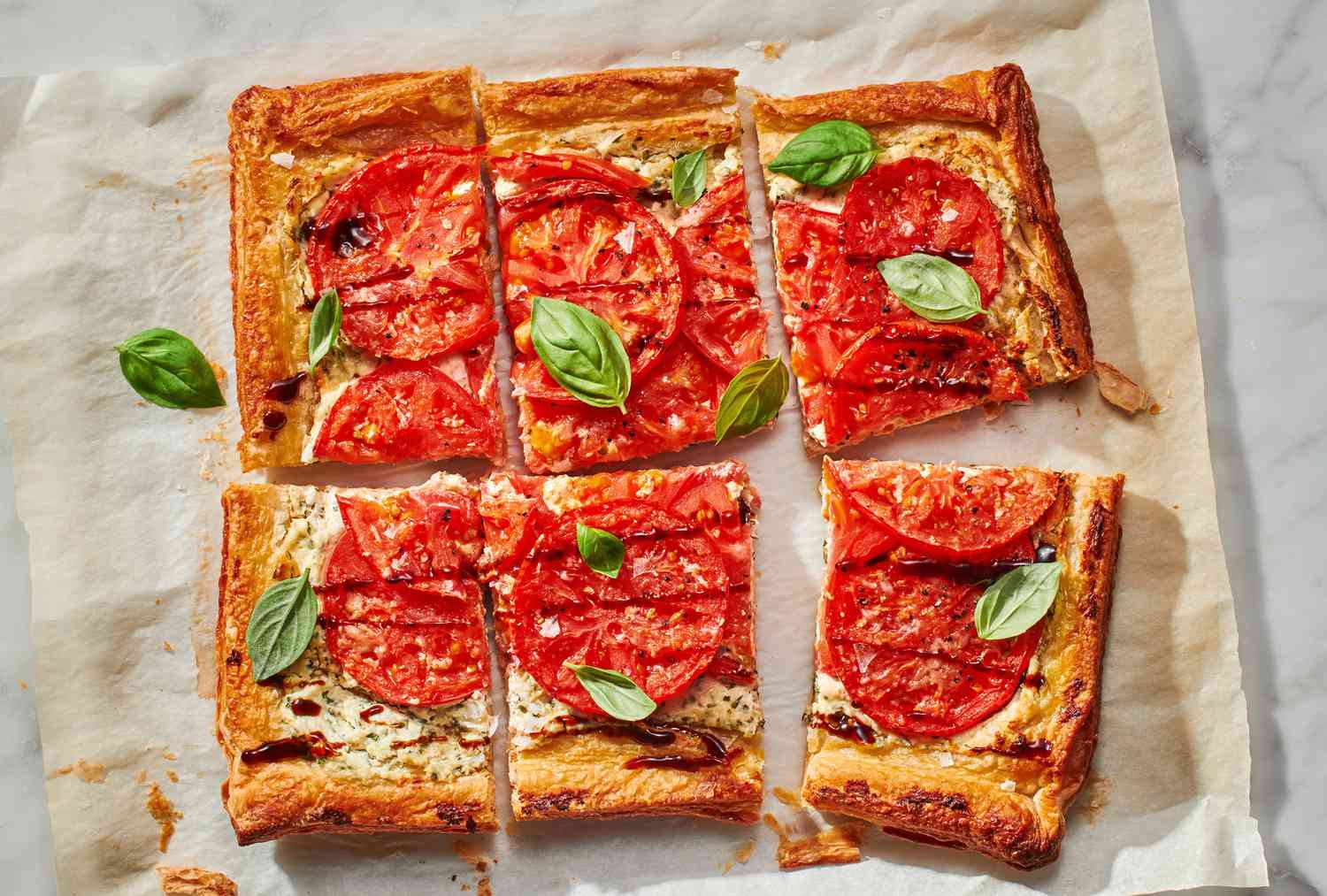 A tomato puff pastry tart topped with fresh basil, balsamic vinegar, grated cheese, salt and pepper