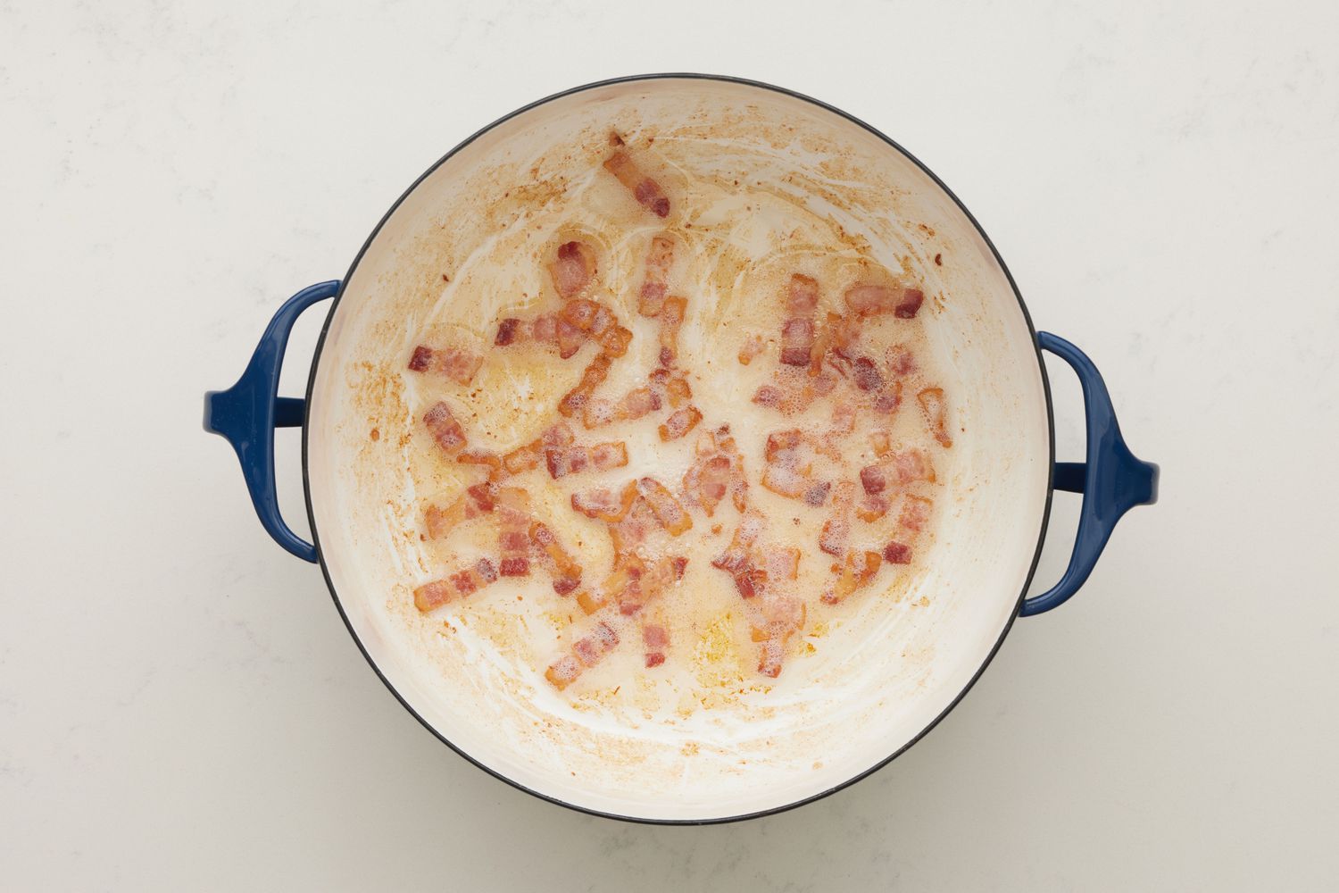 A large dutch oven with chopped bacon cooking