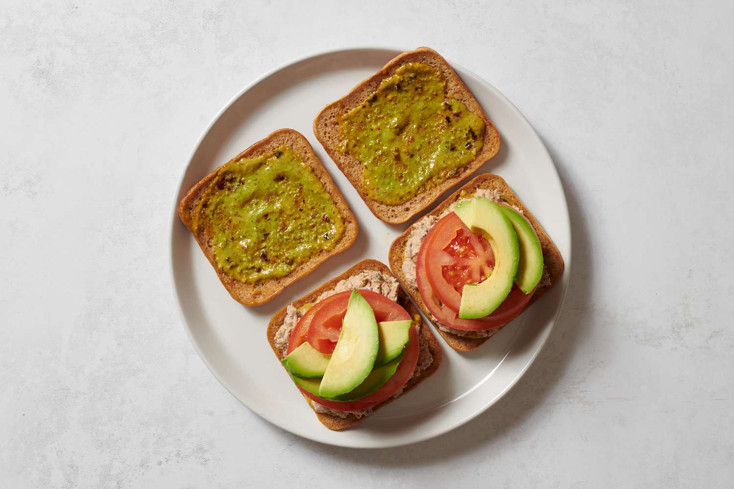 Two slices of bread topped with whipped tuna mixture, tomatoes, and avocado