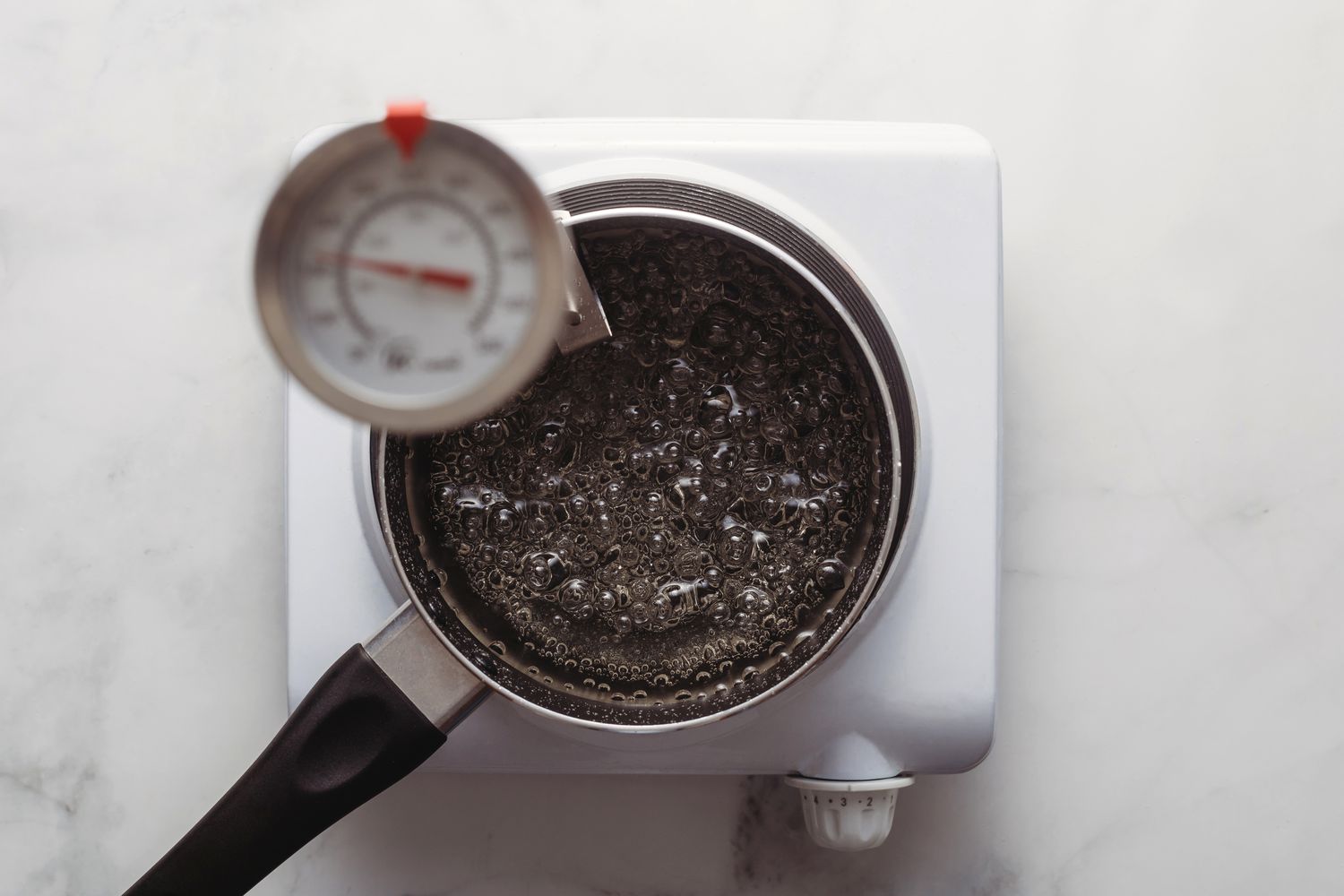 Candy thermometer measuring boiling syrup temperature in a saucepan