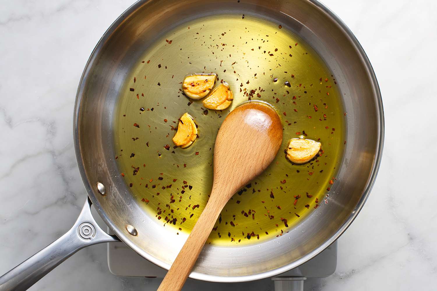 Garlic, oil and red pepper flakes in a pan with a wooden spoon, on a burner 