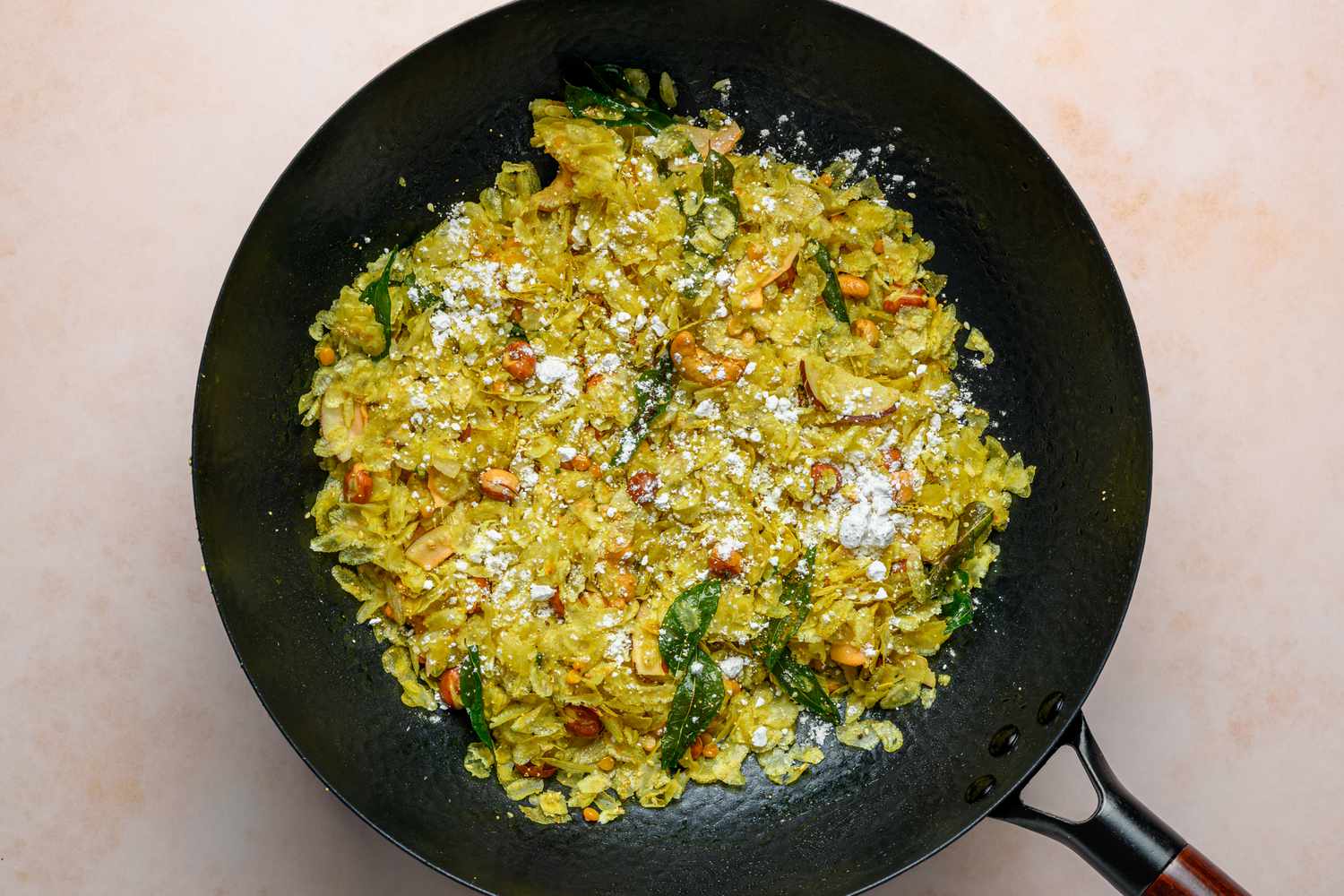 A large wok of poha chivda topped with confectioner's sugar