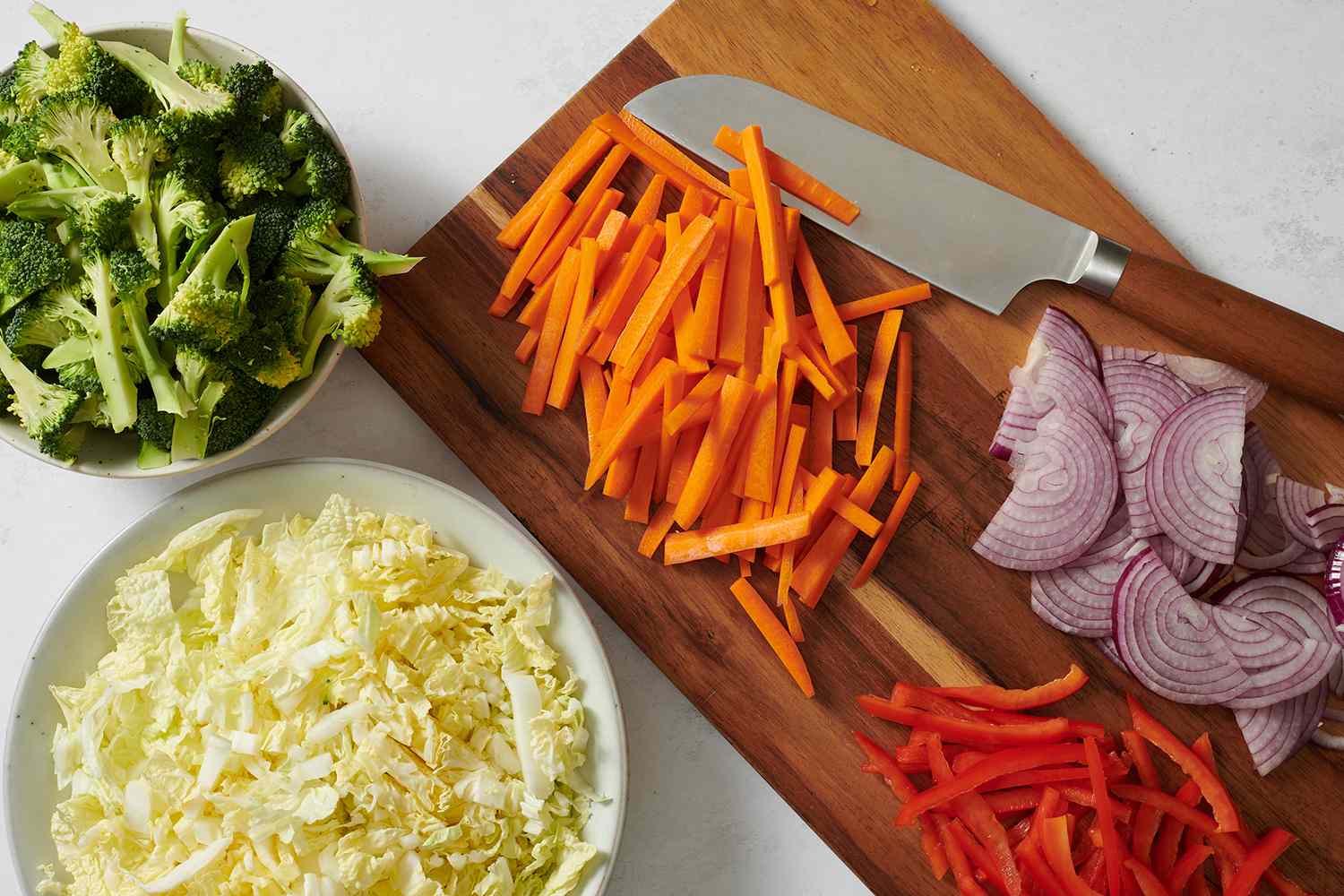 Prepared cabbage, onion, broccoli, carrots, bell pepper, and onion on a cutting board