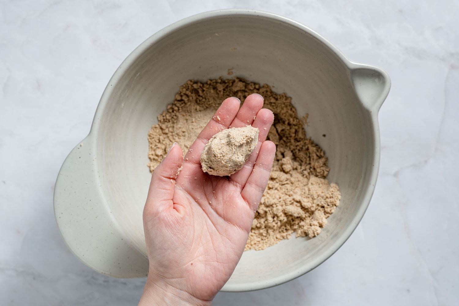 A hand holding a small clump of dough over a bowl of ghee-whole wheat mixture