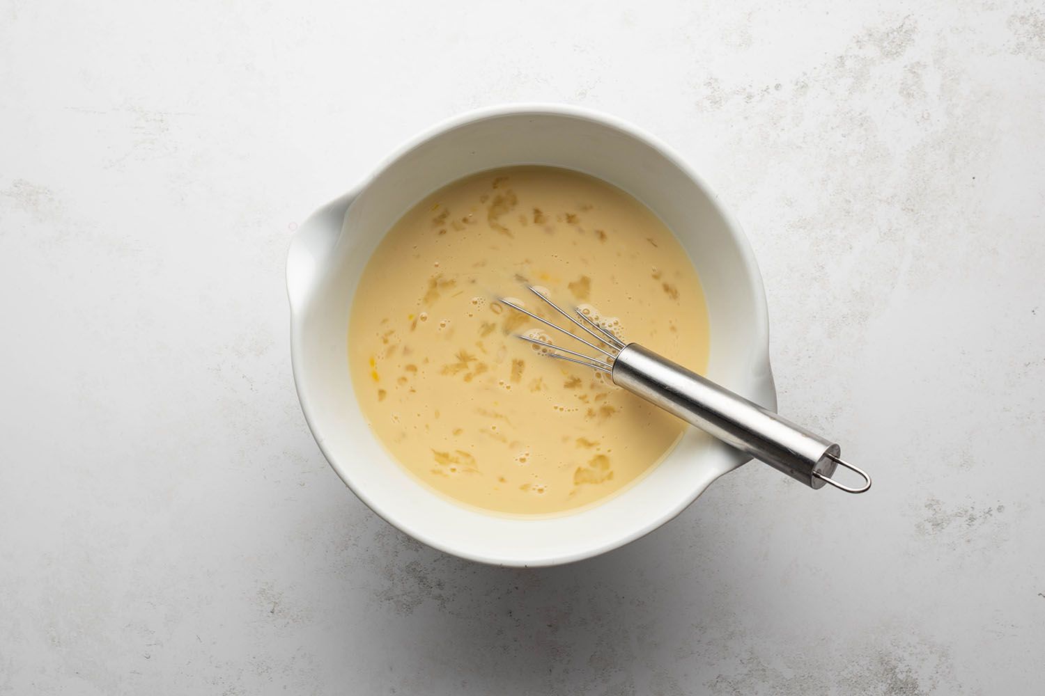 Eggs, milk, vanilla, and maple syrup in a bowl with a whisk 
