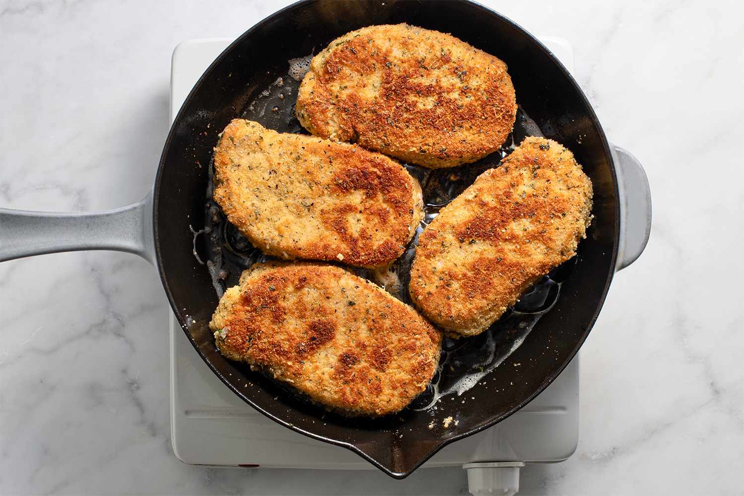 Breaded pork chops cooking in a cast iron skillet on a burner 