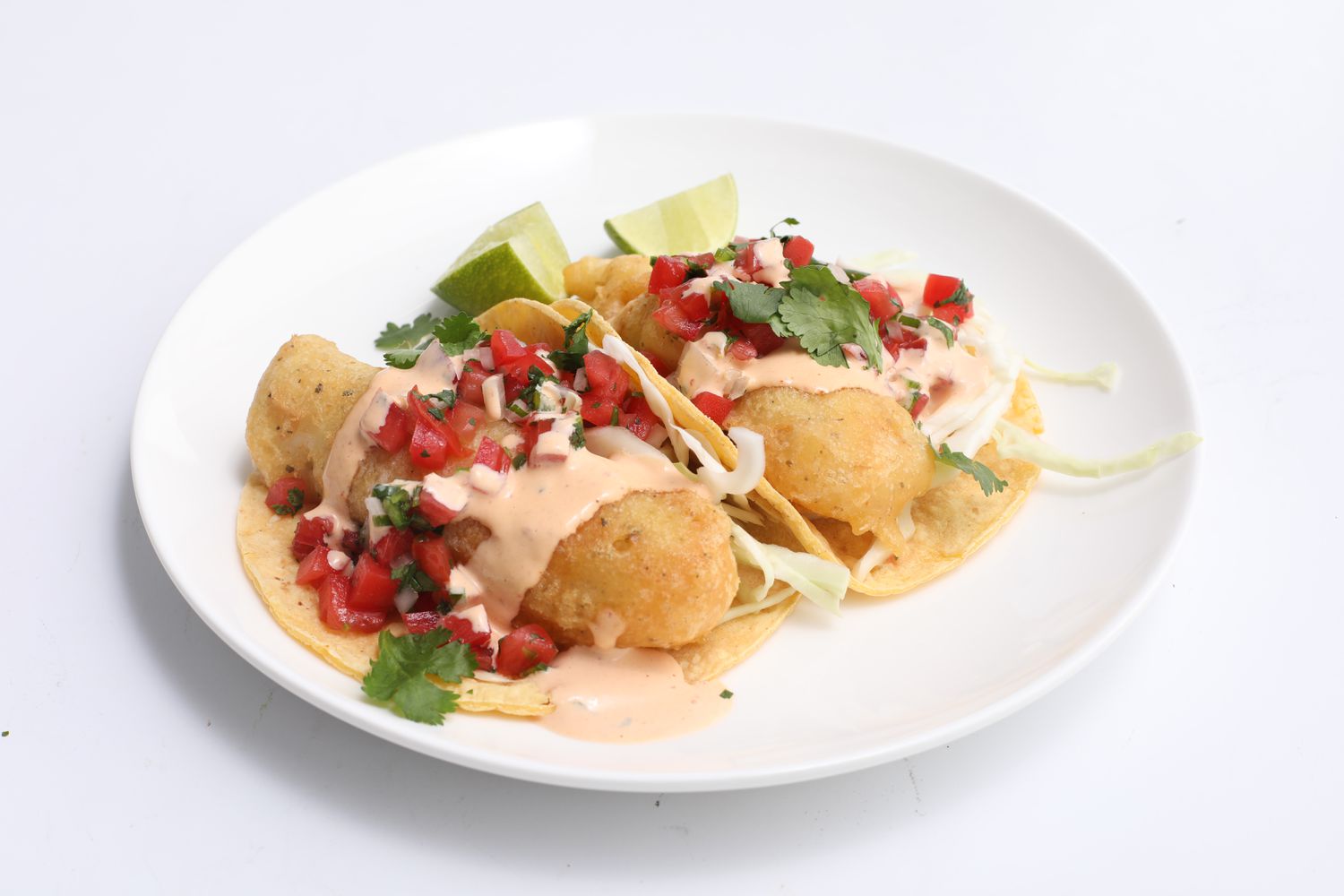 Two fried fish tacos made with corn tortillas and topped with a creamy chipotle sauce and pico de gallo