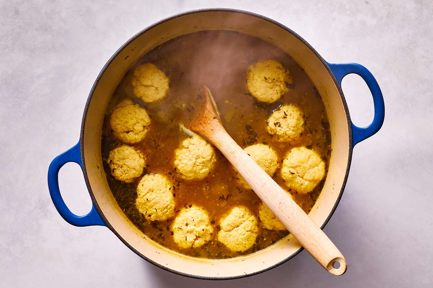 Dumplings cooking in a pot with chicken broth, with a wooden spoon 