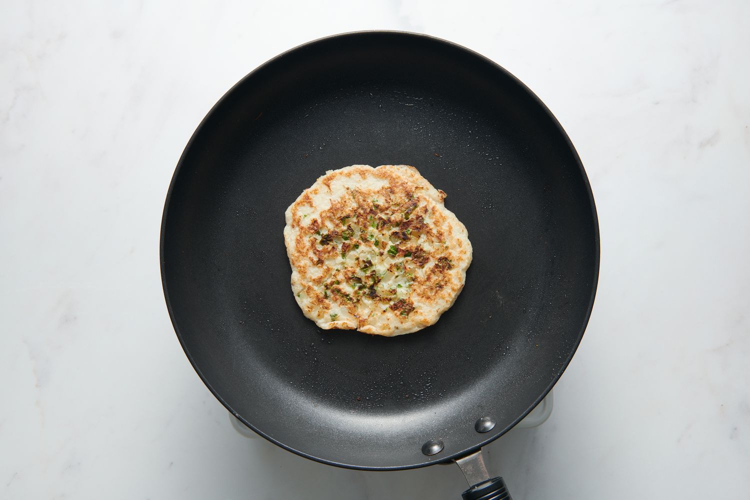 A greased nonstick pan with a cooked, browned uttapam