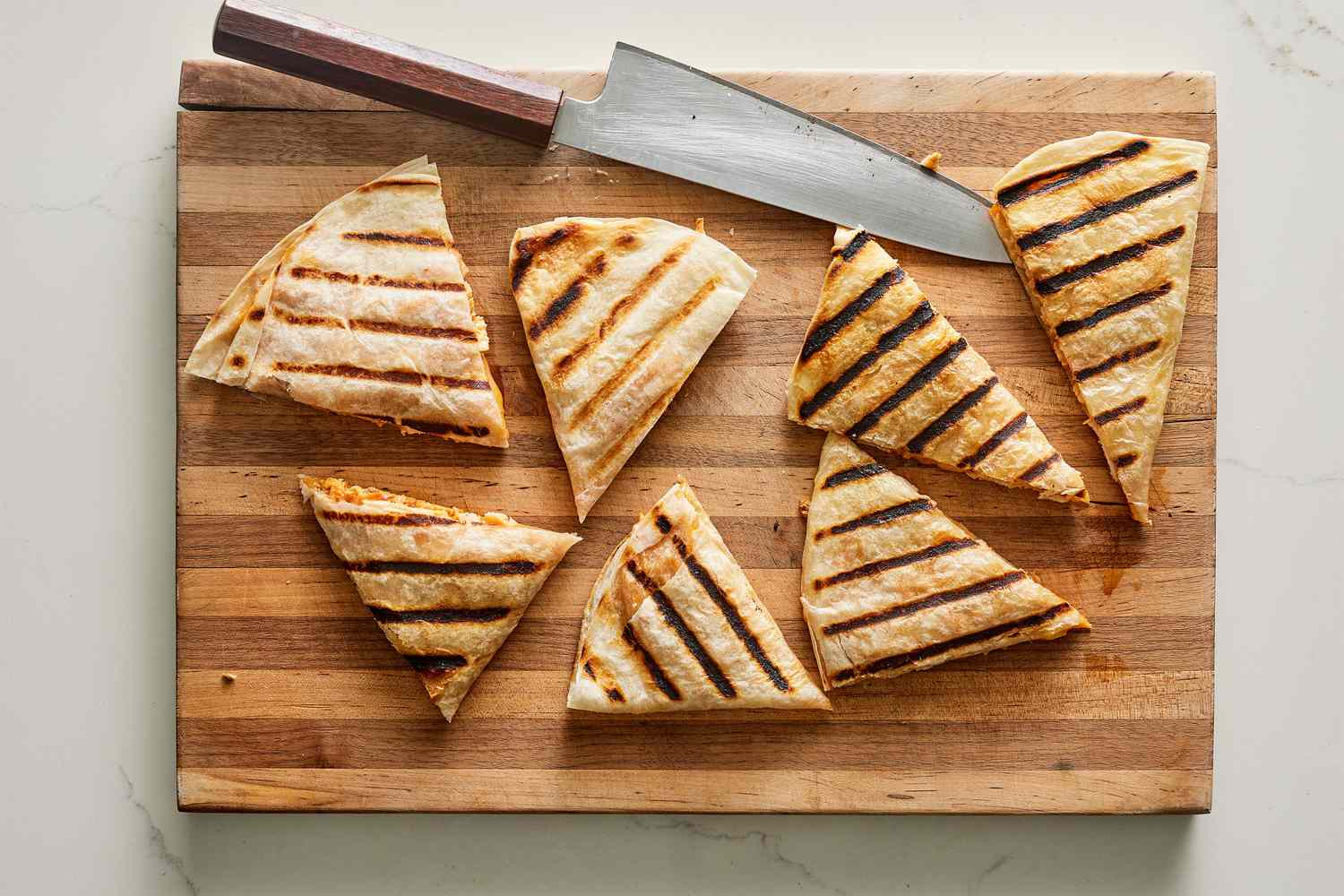 A cutting board with a knife and small wedges of grilled quesadillas
