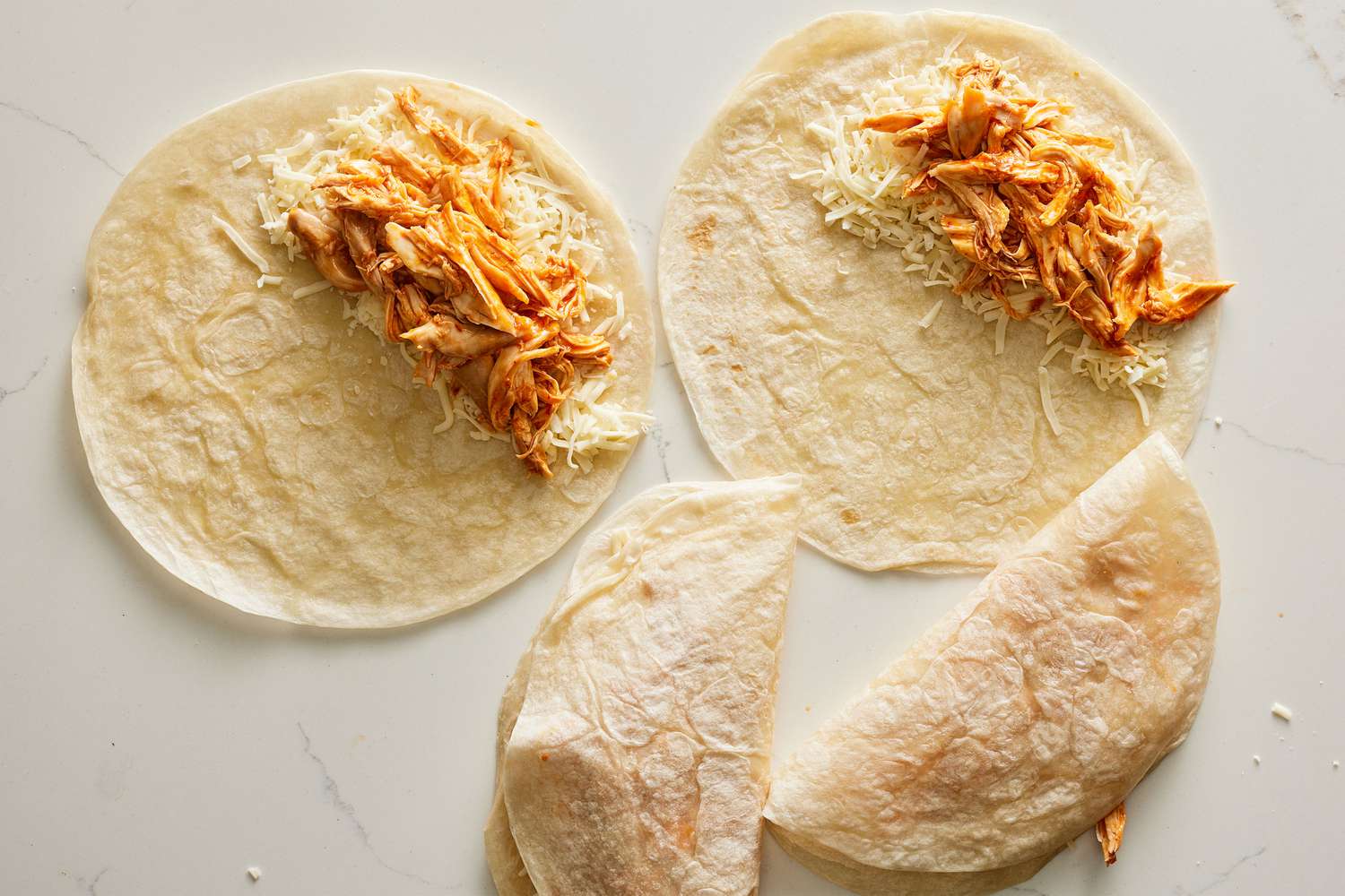 Two tortillas with shredded chicken over shredded cheese, and two folded quesadillas